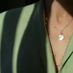 Delikatna biżuteria z pereł i okrągłą zawieszką na zielonej marynarce. Idealny dodatek do styl casual.