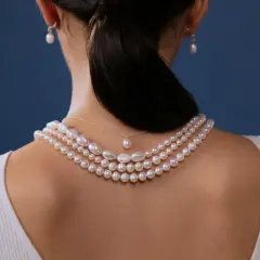 Kobieta z tyłu w białej bluzce, ozdobiona kilkoma naszyjnikami z pereł i kolczykami. Miara pereł podkreśla jej elegancję.