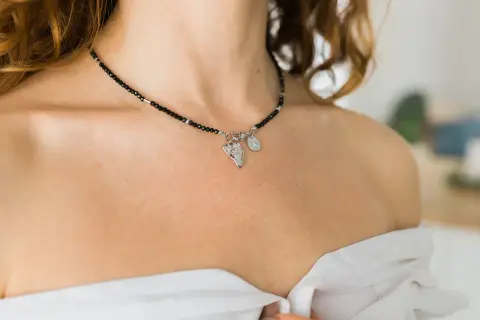 Elegancki kolet z czarnych koralików i srebrnymi zawieszkami, ozdabia dekolt kobiety.