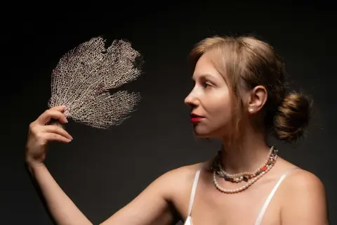 Kobieta z biżuterią i wachlarzem z koralu naturalnego.
