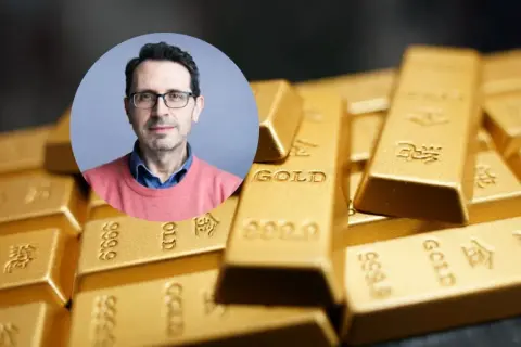 Mężczyzna w okularach na tle sztabek złota. Czy złoto traci na wartości? Analiza eksperta.