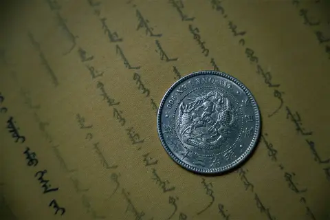 Srebrna moneta bulionowa z wizerunkiem smoka, leżąca na pożółkłym papierze z orientalnym pismem.
