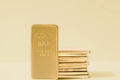 Złota sztabka z napisem "GOLD BAR Fine Gold 999.9" i stos złotych sztabek w tle.