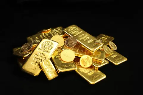 Złote sztabki i monety, w tym słynny Krugerrand, błyszczą na czarnym tle.