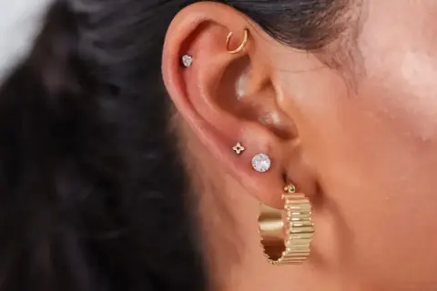 Ucho ozdobione kilkoma kolczykami, w tym subtelnym anti tragus piercing z małym kamieniem.