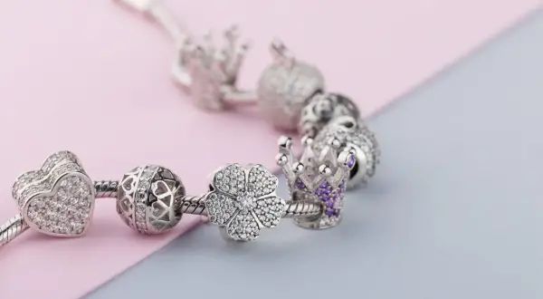 Srebrna bransoletka Pandora z charmsami: serce, ażurowa kula, kwiat i korona z fioletowymi kamieniami. Każdy charms to jak pandora znak zodiaku, symbolizujący coś wyjątkowego.