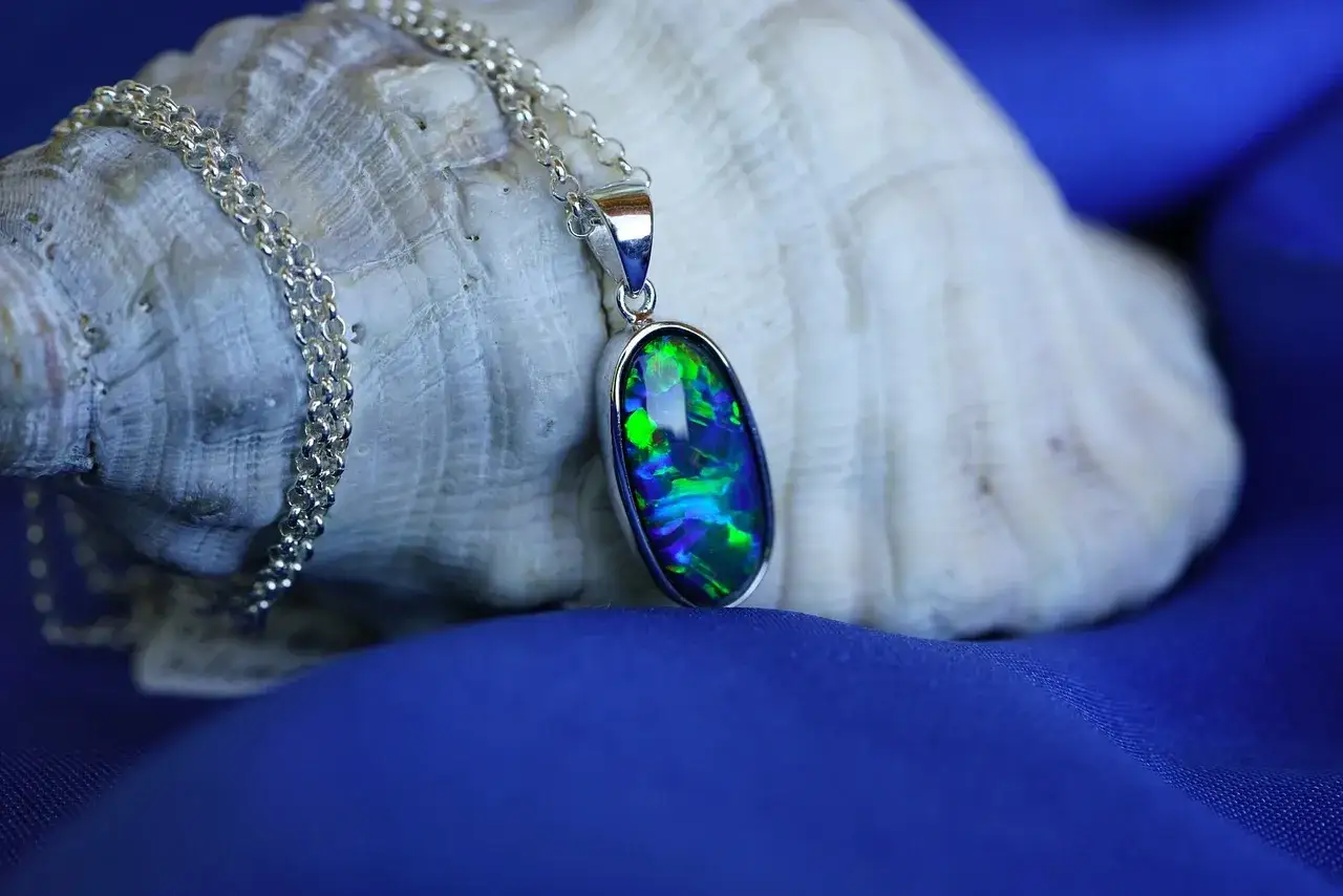Opal w srebrnej oprawie, kamień znak zodiaku, lśni zielenią i błękitem na tle muszli.
