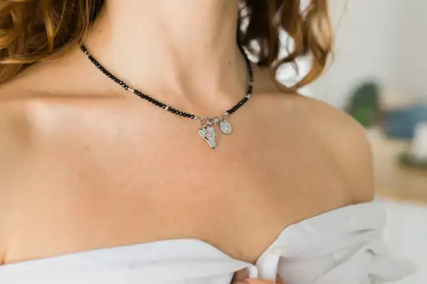 Elegancki kolet z czarnych koralików i srebrnymi zawieszkami, ozdabia dekolt kobiety.