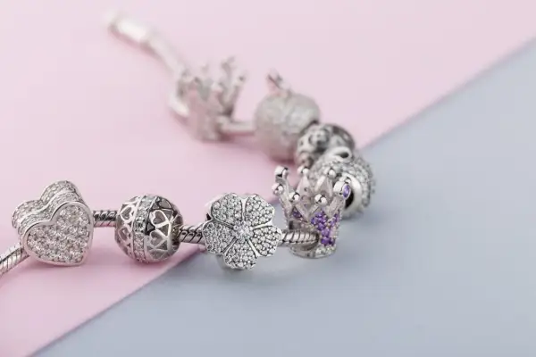 Srebrna bransoletka Pandora z charmsami: serce, ażurowa kula, kwiat i korona z fioletowymi kamieniami. Każdy charms to jak pandora znak zodiaku, symbolizujący coś wyjątkowego.