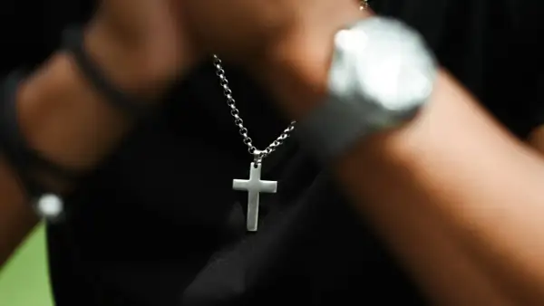Srebrny krzyż na szyi, symbol wiary i nadziei, noszony na czarnym tle.